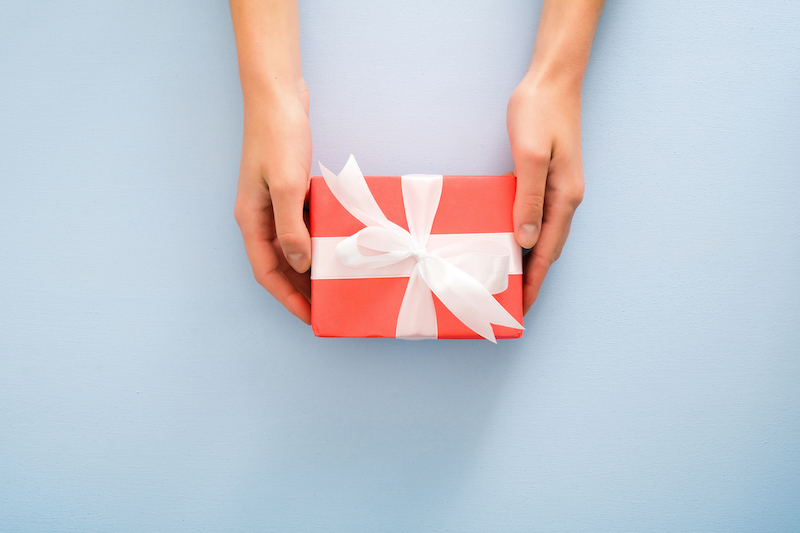 Hands holding a red gift box with a white bow