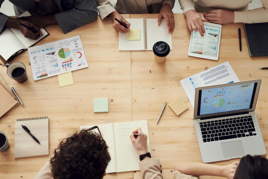 Group of business professionals gathered around a wooden table reviewing documents during a collaborative meeting.