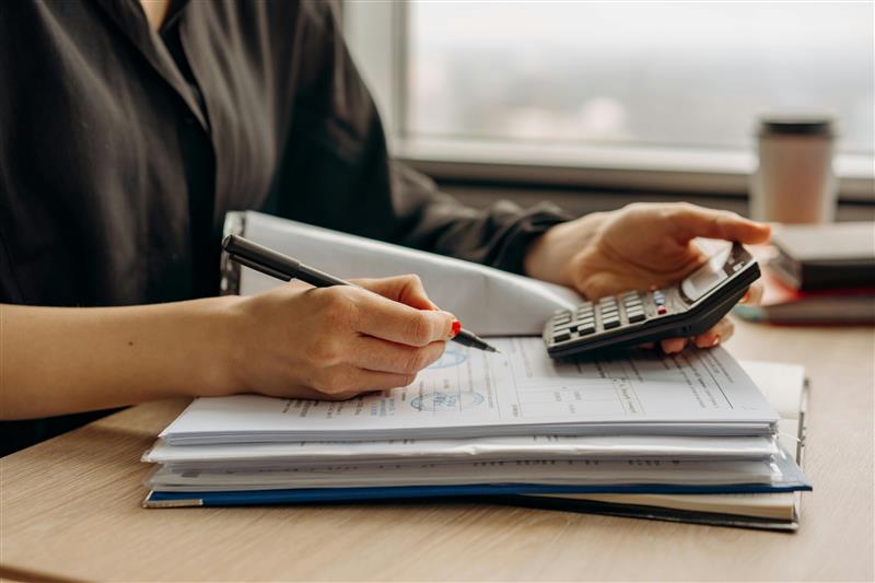 Person using a calculator and reviewing tax paperwork to understand unrelated business taxable income (UBIT) rules for nonprofit organizations.